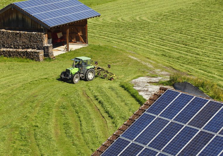 Solar panels mounted on two farm sheds in a field
